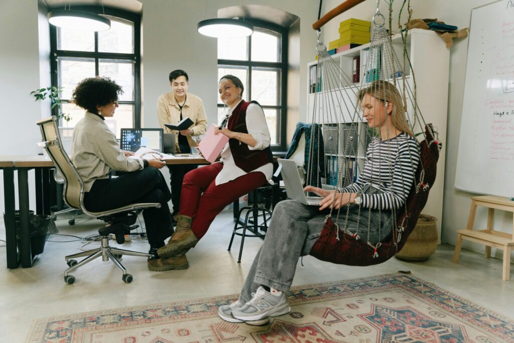 Diverse team engaged in a casual meeting in a modern office setting with laptops and relaxed seating.
